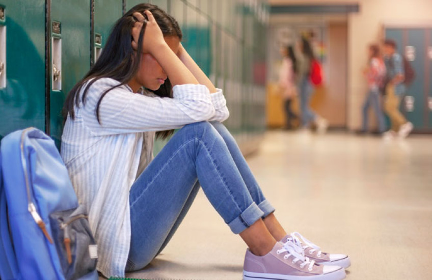 Image of a female high school student sitting on the floor by her locker, head in hands