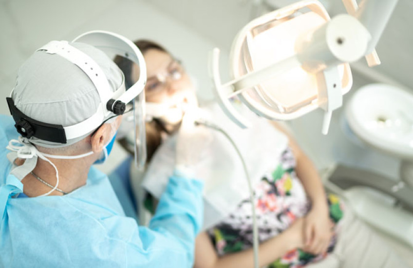 Dentist in full PPE with his hands inside a female patient's open mouth
