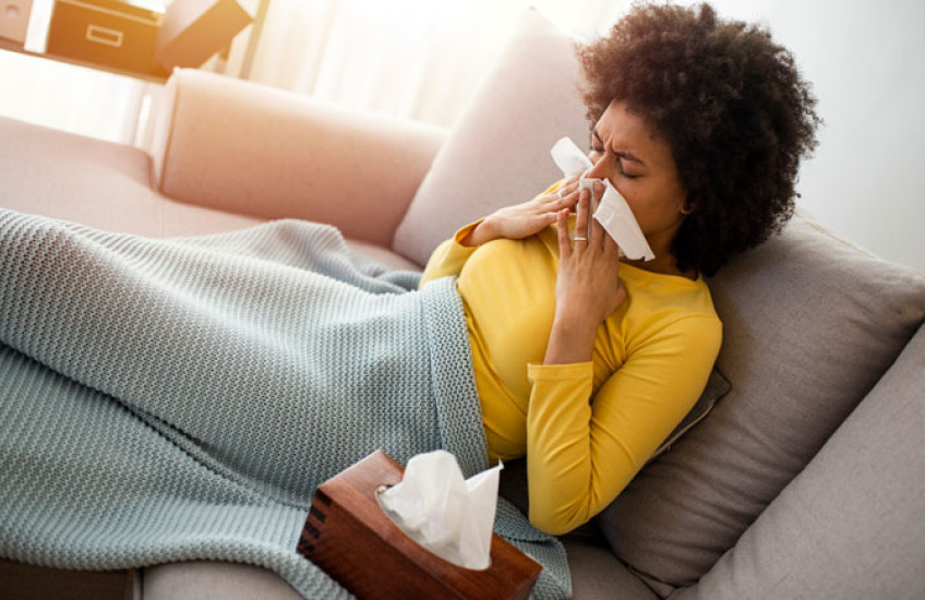 A sick person blowing their nose on a couch