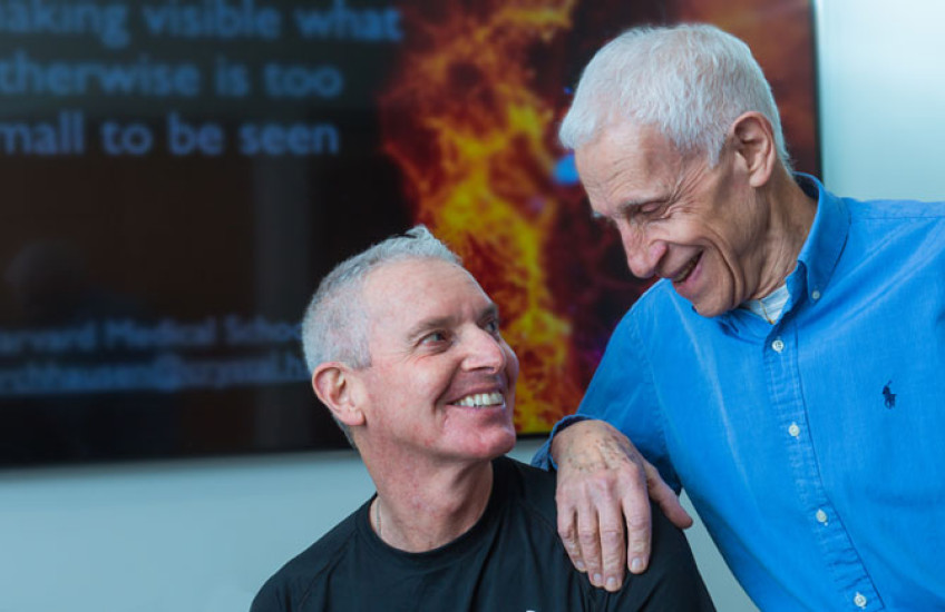 Harrison and Kirchhausen in front of a digital screen with molecular imagery looking into each other's eyes
