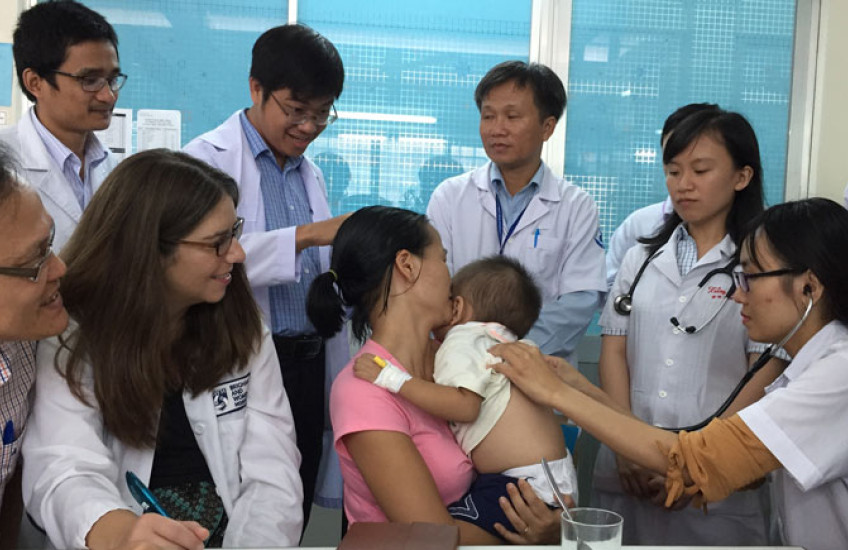 Group of medical students in Vietnam looking on as a baby is examined in clinic, held it its mother's arms.