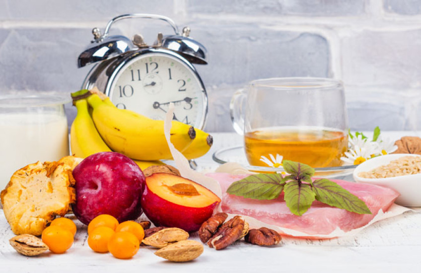 Photo of a bunch of fruit and food with an alarm clock nearby