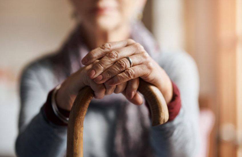 An out-of-focus person with their hands on top of a cane in focus in front of them