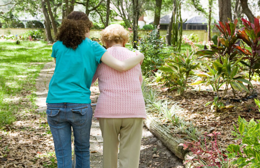 Caregiver walking with elderly woman, photographed from behind 