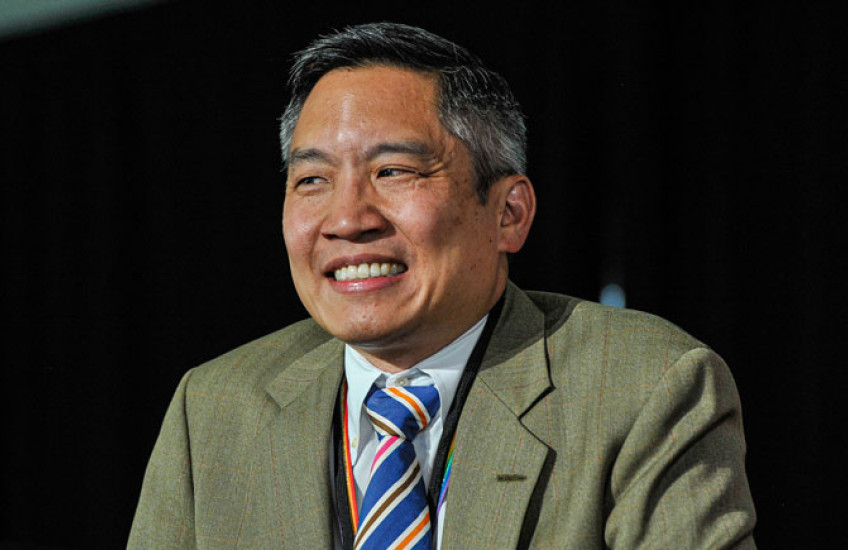Photo of Bernard Chang with a green suit jacket and striped tie, smiling.