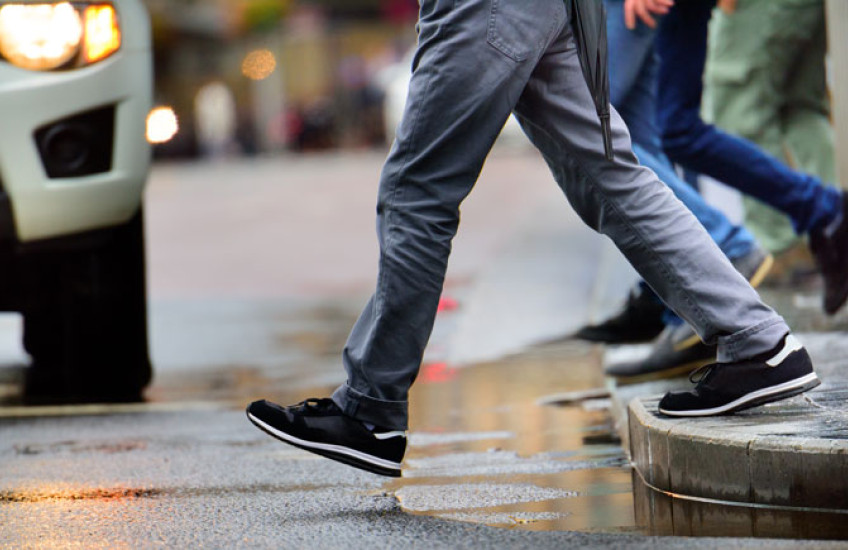 The lower half of a person stepping off a curb to cross the street in front of a car