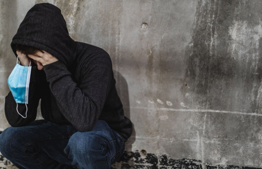 Person with a hoodie on holding their face in their hands and also a mask