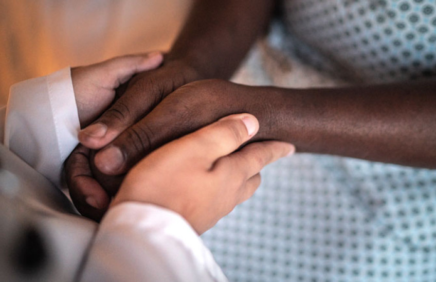 Image of a doctor's hands holding a black hospital patient's hands.  No faces.