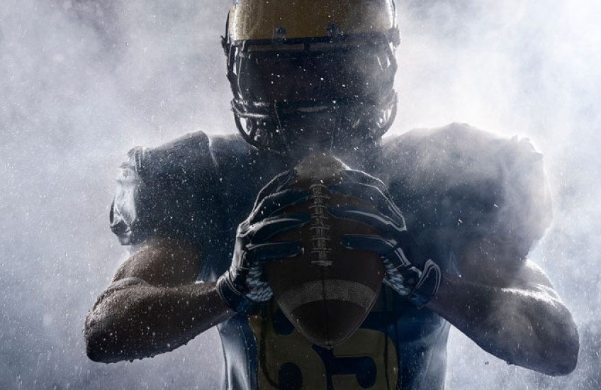 American football player in silhouette gripping a football. 