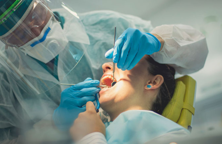 Dentist in full PPE with his hands inside a female patient's open mouth
