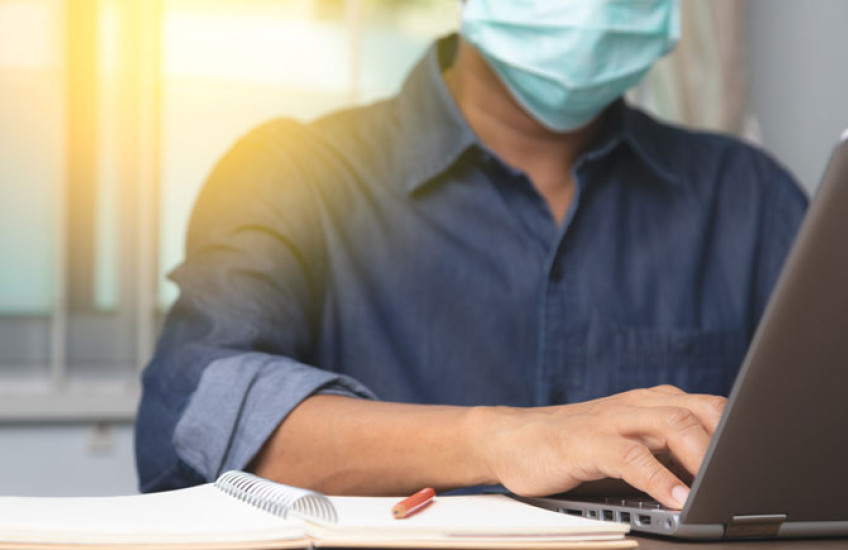 Guy with a mask typing on a laptop computer 