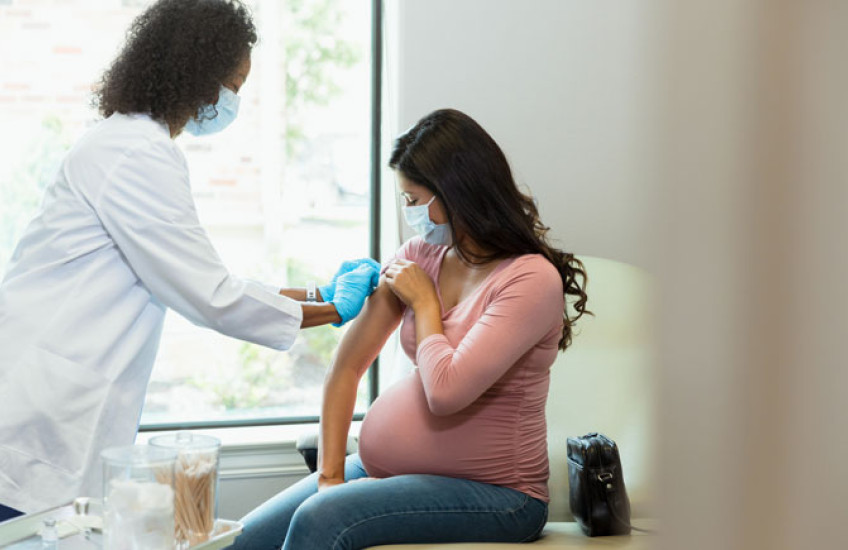 A doctor prepares a pregnant person's arm for a vaccine