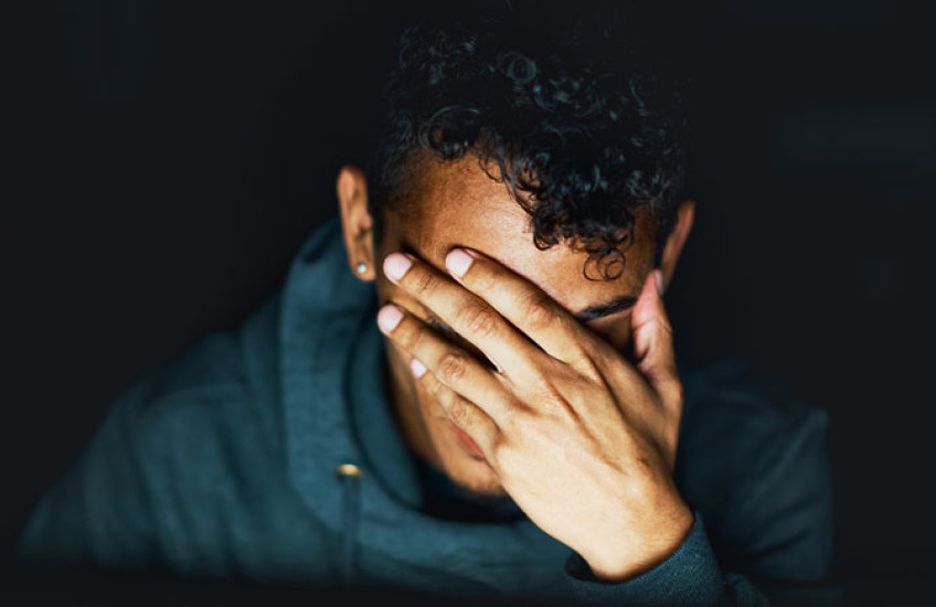 A close up of a person with their hand covering their face against a black background
