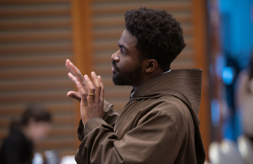 A man in a monk's habit speaks to an audience.
