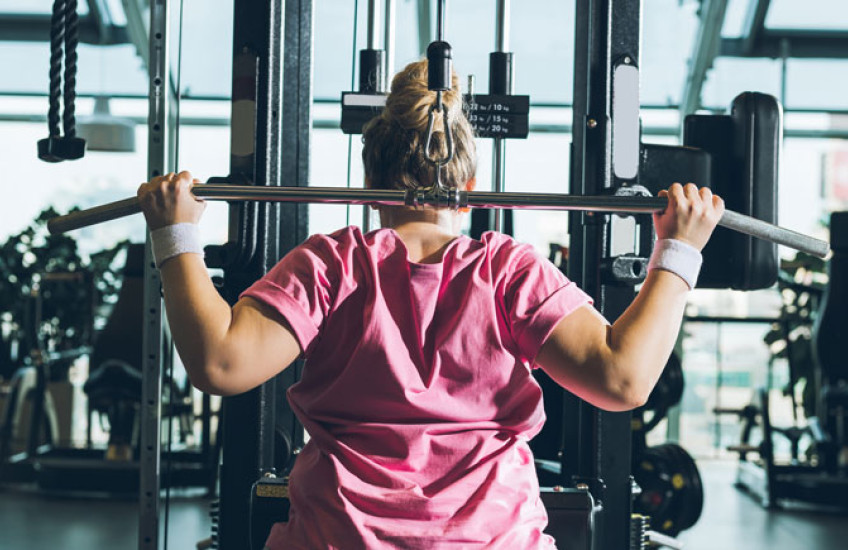 Photo of woman in pink top lifting weights in a gym