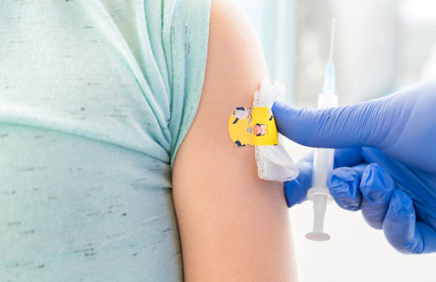 Photo of a child's torso with a bandaid on the arm and a blue glove with syringe