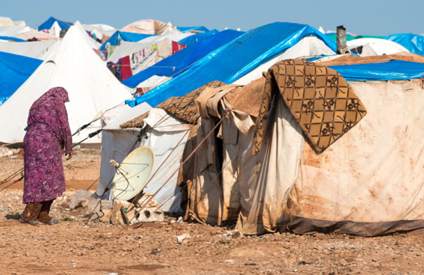 Image of a woman outside a makeshift tent in a Syrian refugee camp