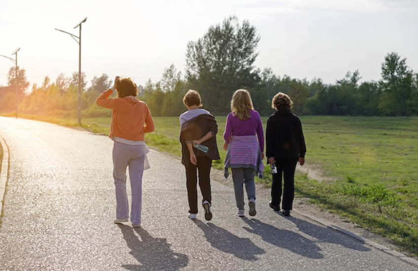Four adult women walking side-by-side on a path surrounded by green grass