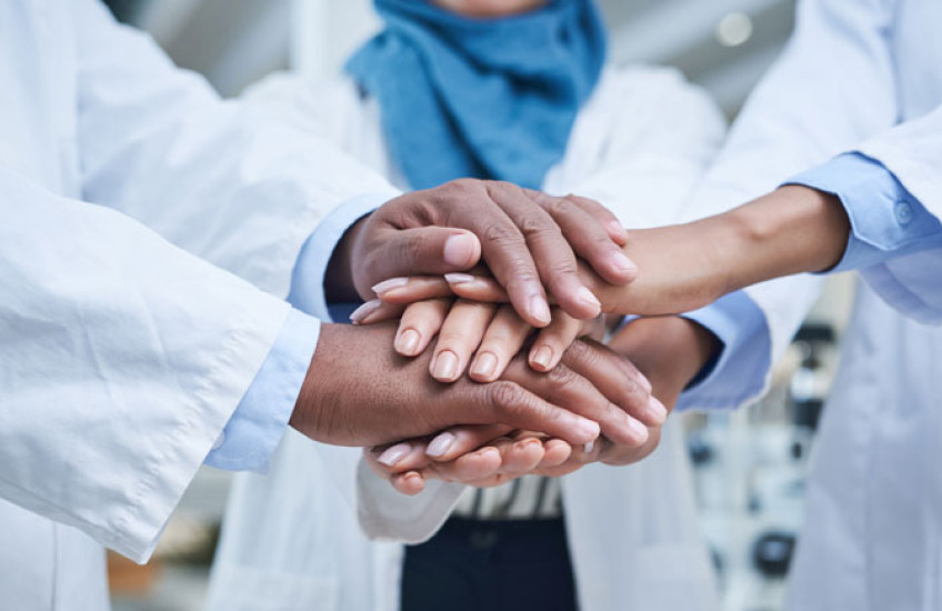 Close up of the stacked hands of three physicians with different ethnicities in solidarity.