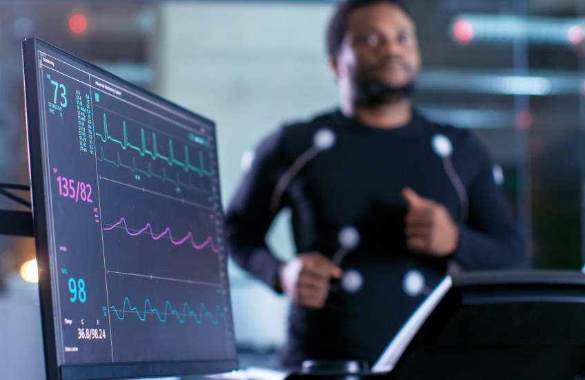 Blurred image of a man on a treadmill with electrodes attached and connected to a heart monitor in a research lab