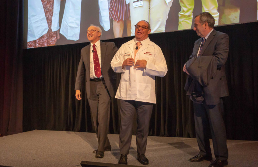 Alex Blavatnick (center) receives the gift of an HMS white coat from HMS Dean George Daley (left) and Harvard President Larry Bacow. 