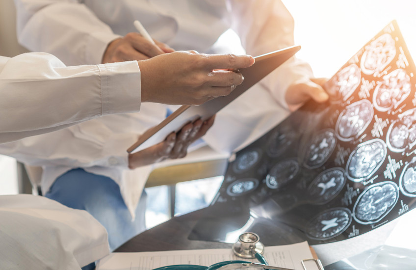 Closeup of the hands of two people wearing white lab coats examining medical images of a patient’s brain.