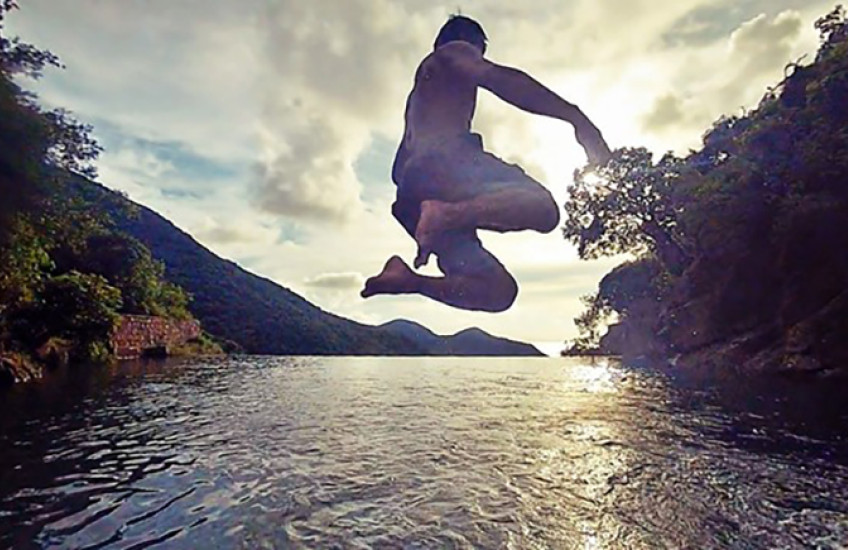 Will Chan jumping into a body of water, backlit