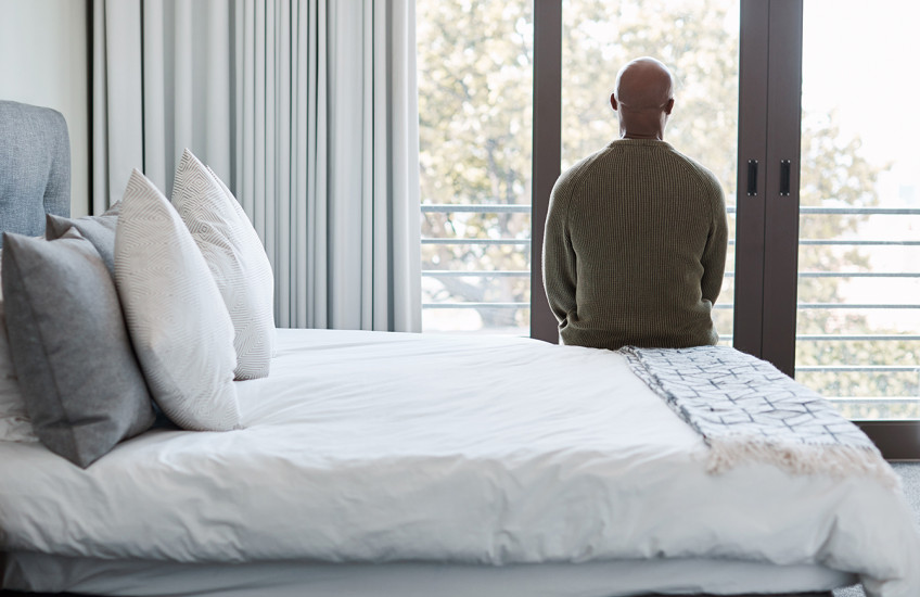 Rearview shot of a mature man looking through a window in a bedroom.
