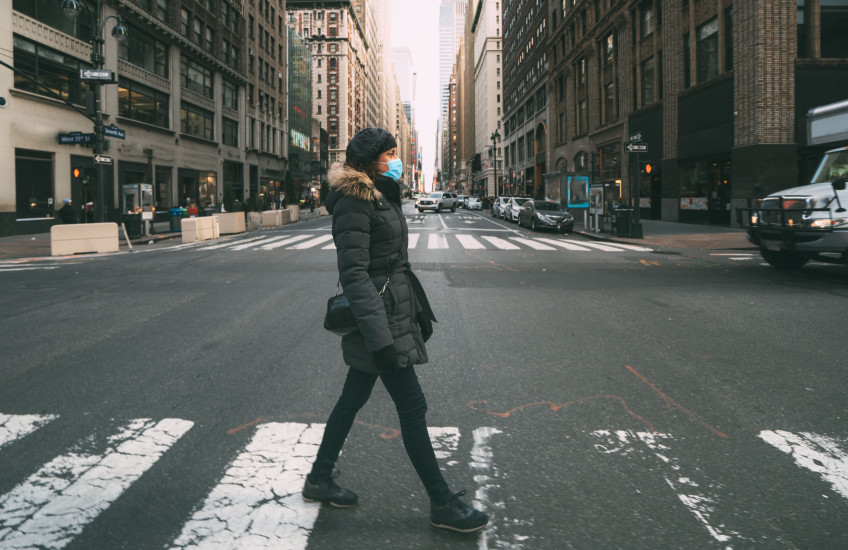 A woman in a surgical mask crossing a street in mid-town Manhattan