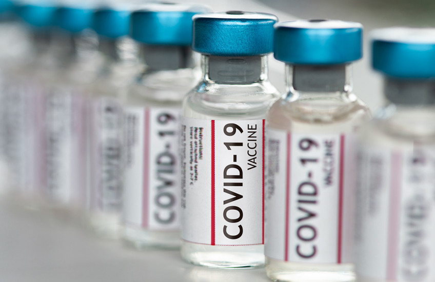 A row of vials labeled COVID-19 vaccine sits on a shelf.
