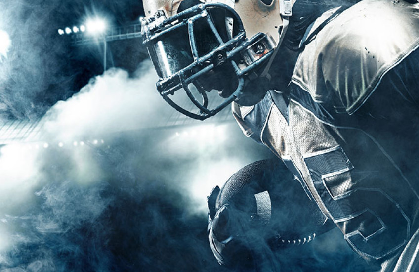 A running back holds the ball in a dimly lit arena.