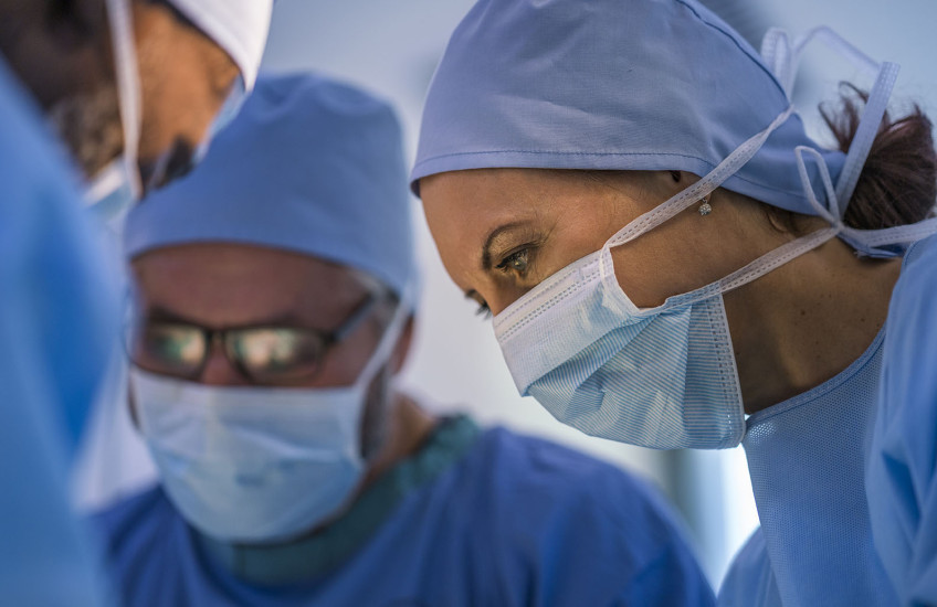 A woman in a surgical mask with men in surgical masks out of focus in the background.