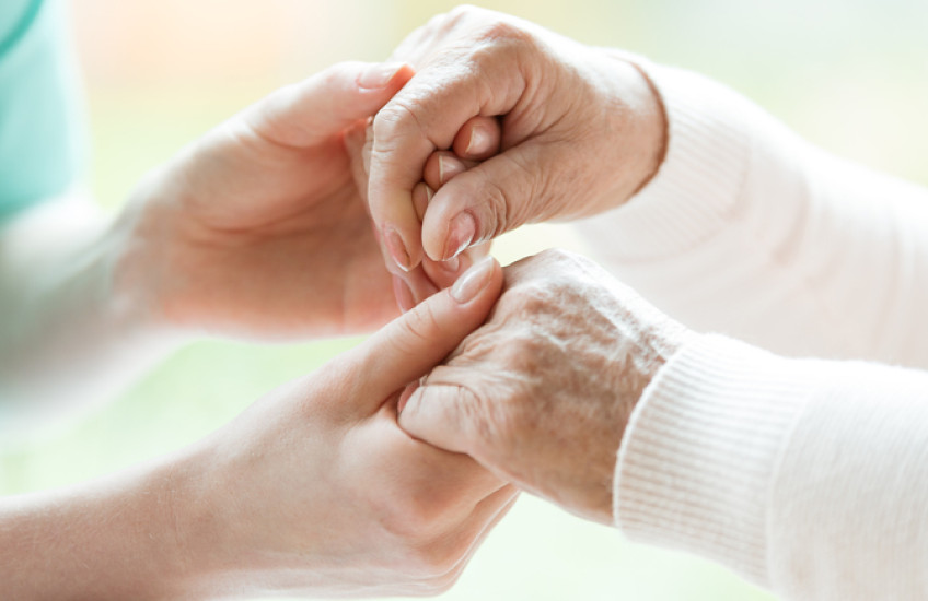 Image: a caregiver holding hands with a hospice patient