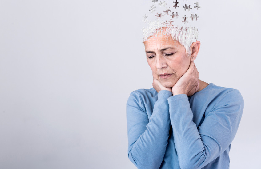 Photo of a distressed woman with short gray hair with illustration puzzle pieces flying out of the top of her head