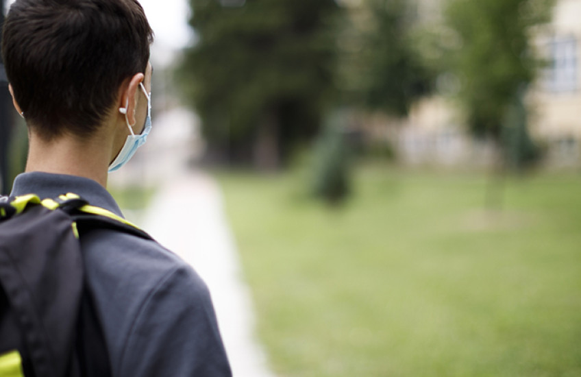 Rear view of a child with backpack and mask on facing a schoolyard