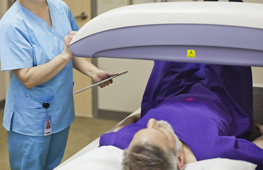 Photo of a gray-haired man lying on an exam table while a technician adjusts a scanning machine over him