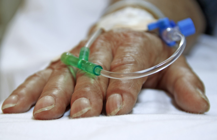 Photo of a surgery patient's hand resting on a bed, with tubes going into the hand