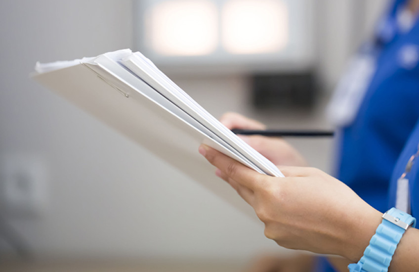 two people in scrubs, heads not shown, review a sheaf of papers indicating a patient file