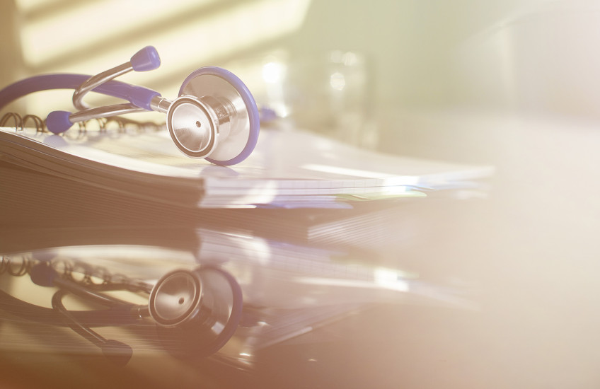 Photograph with soft filter; a stethoscope on a desk with a reflection on the desktop, no doctor there