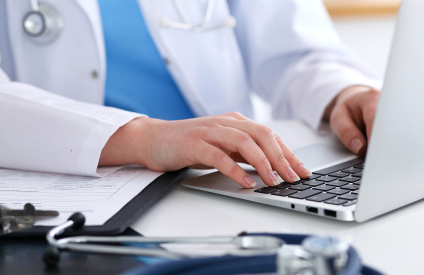 Photo of a physician's hands typing on a keyboard; stethoscope on desk