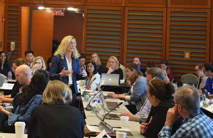 Crowded room of adult learners at tables with laptops with a woman instructor standing in the middle