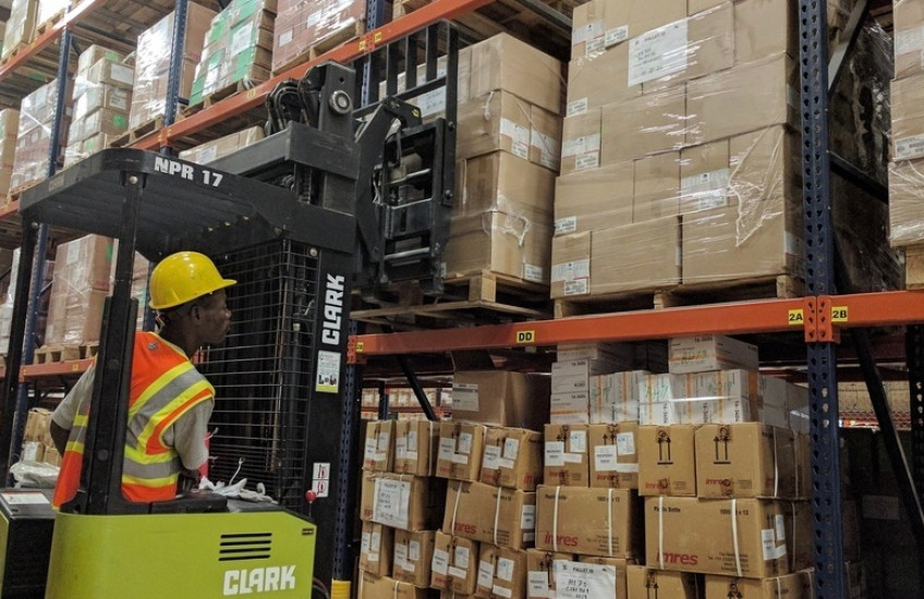A man operates a forklift loaded with boxes in a warehouse.
