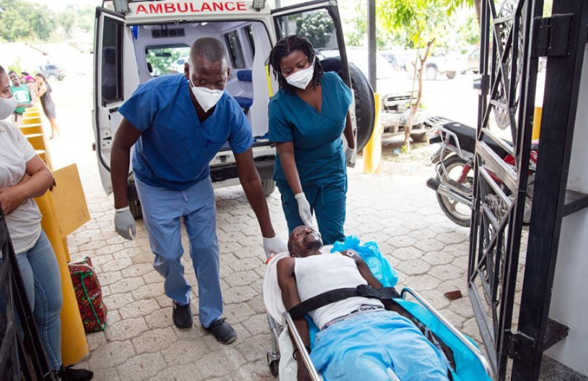 Two emergency clinicians wheel a  man on a gurney from an ambulance into a hospital entryway in Haiti
