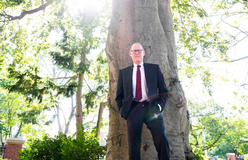 Paul Farmer stands against the front of a tall tree.