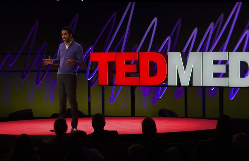 A man speaks on a stage, standing in front of a sign that says TEDMED.