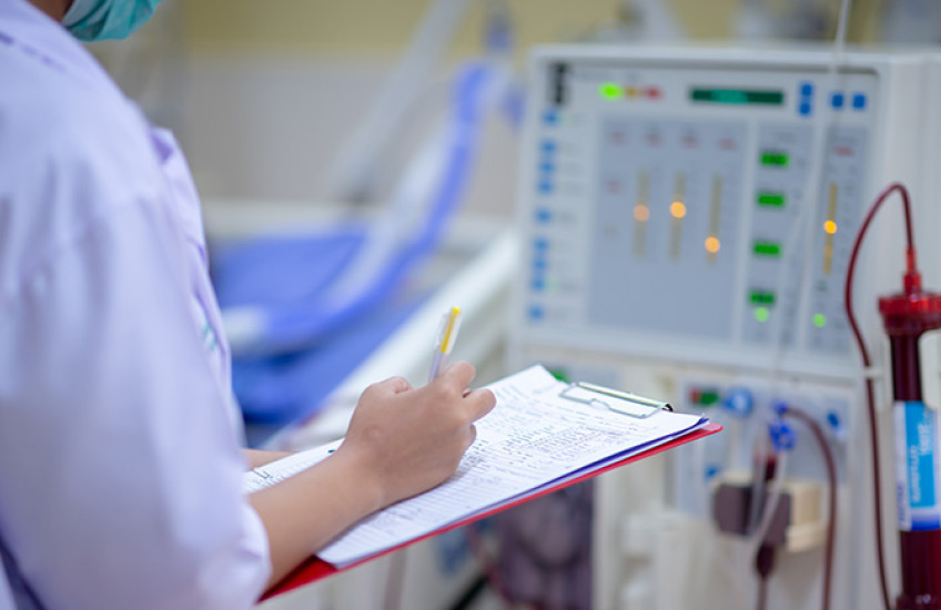 nurse with clipboard checking dialysis machine