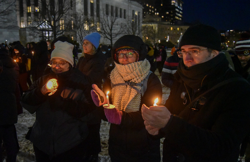 People outdoors on a snowy night wearing warm clothes and holding glowing candles