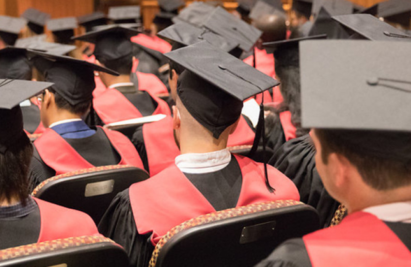 View of back of master's graduates in graduation attire seated in martin conference center