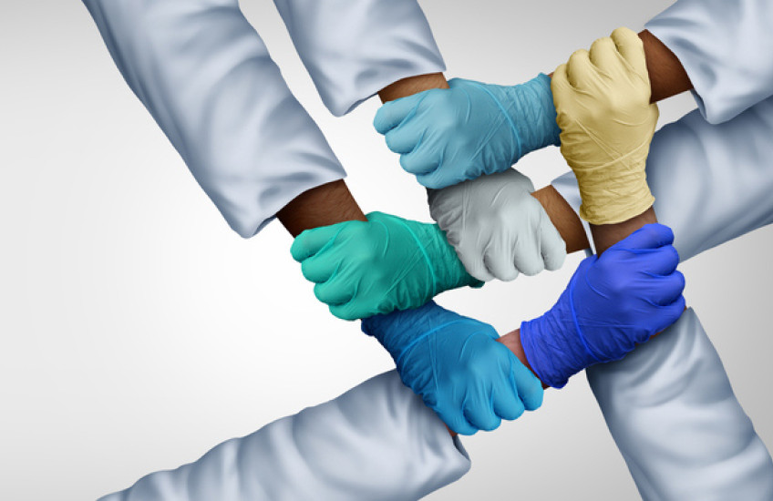 Photo of five gloved hands grasping alternating forearms of different skin colors