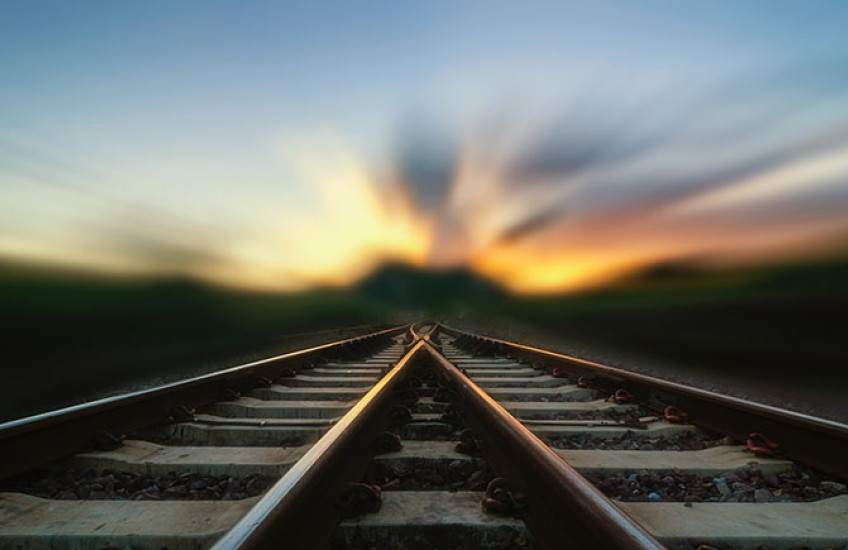 Two train tracks merge in a blurry sunset.